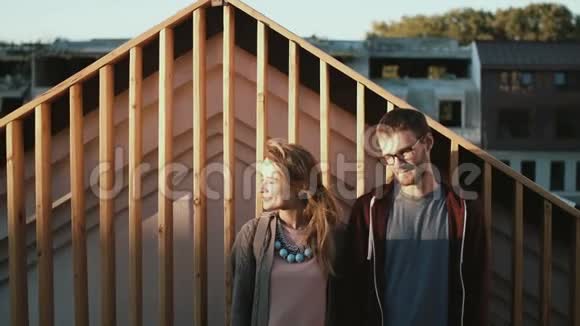 年轻漂亮的一对夫妇站在屋顶上一起向旁边看男人和女人一起在夕阳下散步视频的预览图