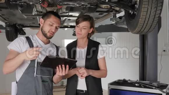 汽车的服务人员与客户交谈师傅在平板电脑上展示技术状况汽车修理工展示视频的预览图