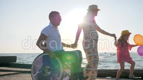 怀孕暑假残疾男人怀孕女孩和带气球的孩子在沙滩背着背光散步爸爸视频的预览图