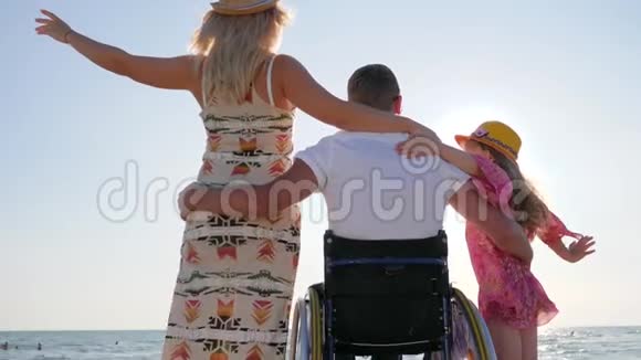 丈夫在轮椅上拥抱妻子和背光小女孩残疾拥抱妻子和女儿无效视频的预览图