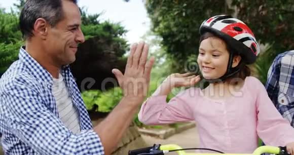 女孩坐在自行车上而快乐的父母给她击掌拥抱她视频的预览图