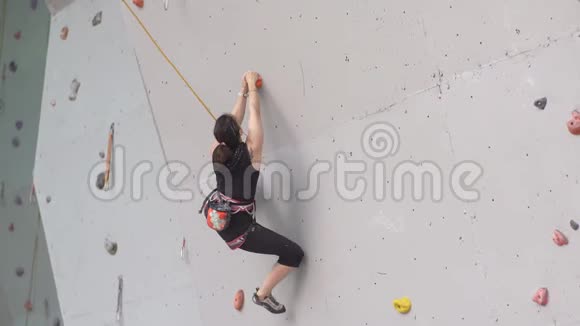 年轻女子在室内攀岩墙上锻炼在攀岩墙上训练登山者女孩锻炼了摇滚视频的预览图
