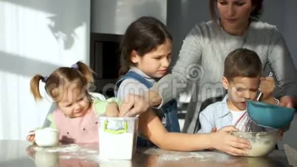 一个由两个成年人和三个孩子组成的快乐家庭在厨房里揉面团爸爸妈妈帮助孩子们笑视频的预览图
