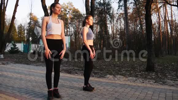 活跃的运动女孩在日落时在绿色公园的混凝土跑道上做腿部热身运动年轻女性跑步者视频的预览图
