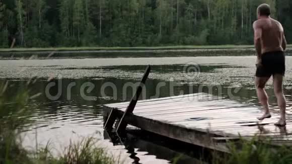 白种人成熟的男人从湖边的木墩上跳下来视频的预览图