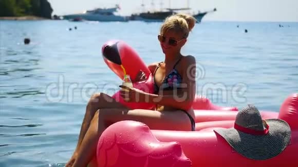 美丽的年轻女子在阳光下放松在土耳其法塞利斯海滩上的红色充气天鹅上视频的预览图