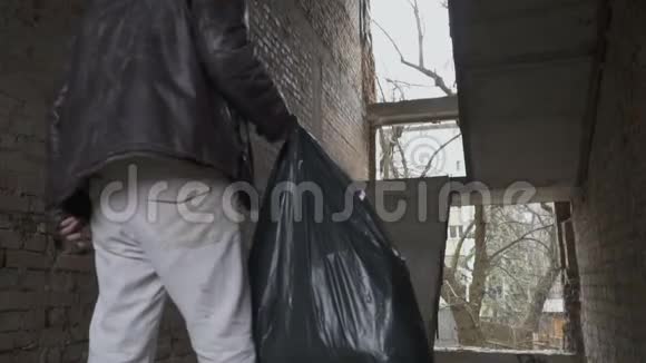 肮脏的流浪汉拿着垃圾袋上了废弃大楼的楼梯视频的预览图