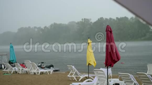 夏雨雷雨强降雨在空旷的沙滩上河边孤独的空的空的阳光的沙滩伞的视频的预览图