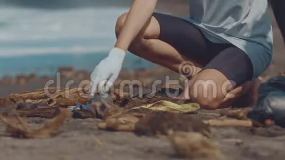 特写志愿者坐在沙滩上捡垃圾清洁员把海边的垃圾收集成黑色视频的预览图