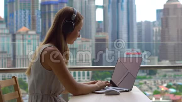 年轻女性自由职业者在阳台上的笔记本电脑上工作背景是一个充满摩天大楼的市中心视频的预览图