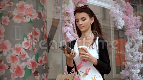 漂亮的女孩带着购物和一杯咖啡站在陈列柜附近视频的预览图