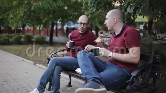 晚上下班后在公园长椅上吃零食两个男人正在公园的长凳上吃三明治喝着杯子里的咖啡视频的预览图