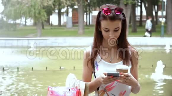 女人坐在喷泉附近的街道上盯着电话视频的预览图
