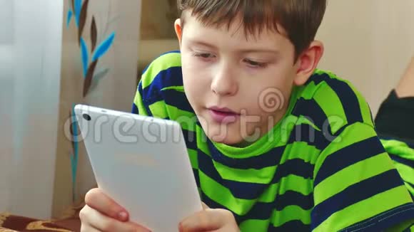 小男孩躺在床上玩平板电脑男孩青少年社交媒体互联网上的平板电脑在室内儿童视频的预览图