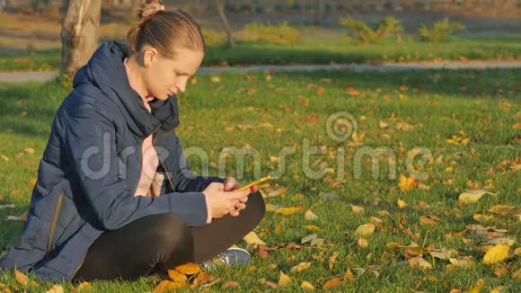 女孩秋在公园里坐在草地上从电话里发短信视频的预览图