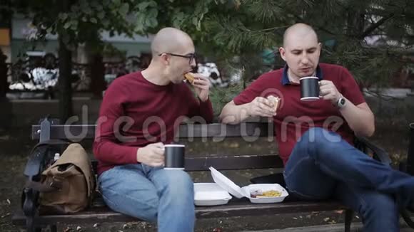 晚上下班后在公园长椅上吃零食两个男人正在公园的长凳上吃三明治喝着杯子里的咖啡视频的预览图