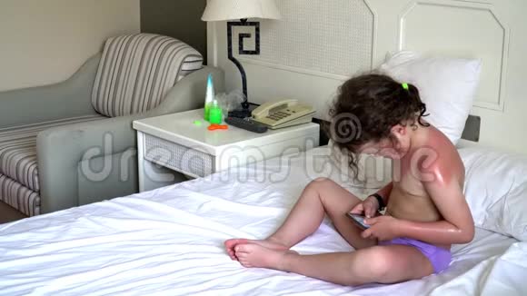 小女孩在白床上玩智能手机视频的预览图