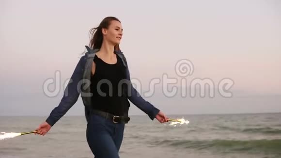 日落时分年轻美丽的女人在海边奔跑双手拿着燃烧的闪闪发光的蜡烛慢动作视频的预览图