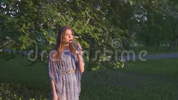 美丽的女性徒步旅行者在日落时在森林里饮水穿裙子的女孩从塑料瓶里喝凉水视频的预览图