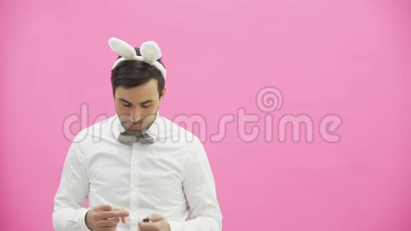 站在粉红色背景上的漂亮男孩穿着白衬衫的时候拿着胡萝卜想烧它视频的预览图