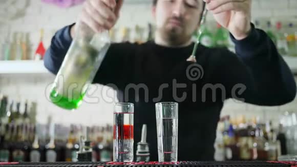 男性酒保制作有色饮料在柜台上用酒精将明亮的酒从瓶子倒入玻璃杯中视频的预览图