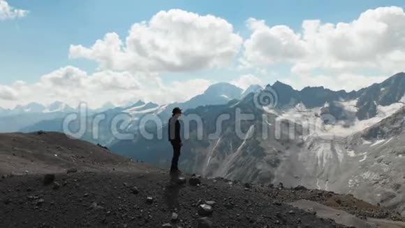一个戴着帽子戴着墨镜站在悬崖上被白雪覆盖的高加索山脉包围着的人周围视频的预览图