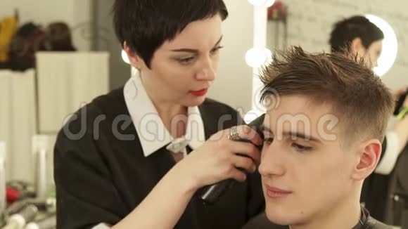 理发店里的理发师用电动剃须刀剪头发女理发师和客户一起工作视频的预览图