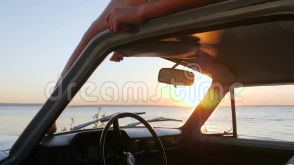 年轻女性在户外的屋顶汽车上放松女性在背景海慢动作中享受复古车的自由视频的预览图