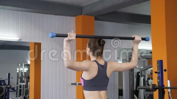 年轻漂亮的运动女孩在健身房举起杠铃棒肩部锻炼背面观看60英尺视频的预览图