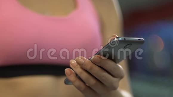 积极的女性在健身房滚动智能手机屏幕使用体育移动应用程序视频的预览图