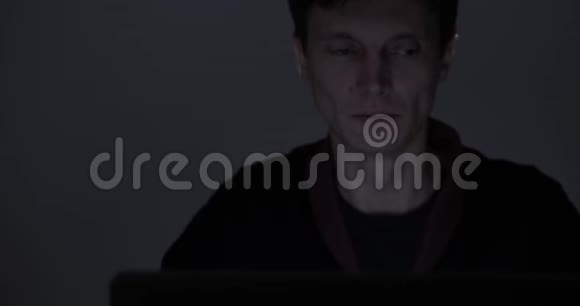 一个疲惫的男人深夜在黑暗的房间里用笔记本电脑工作的肖像视频的预览图