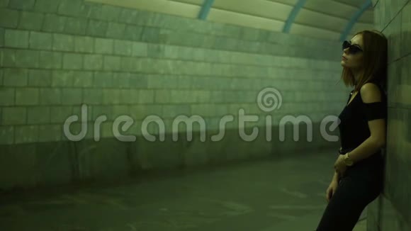 戴眼镜的漂亮时髦女孩站在靠近墙的人行地下通道里视频的预览图