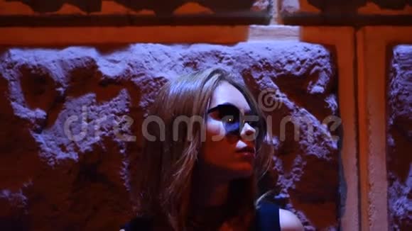 在红灯区的背景下戴眼镜的时髦女士站在墙边视频的预览图