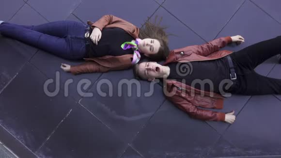 可爱的年轻夫妇穿着浅棕色夹克躺在深色瓷砖地板上视频的预览图