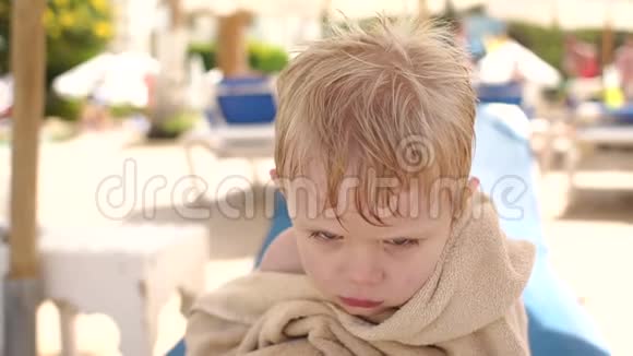 泳池边一个穿着沙滩毛巾的悲伤男孩的肖像视频的预览图