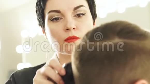 与理发店的客户合作的女发型师女性理发师用电动剪雄性头发视频的预览图