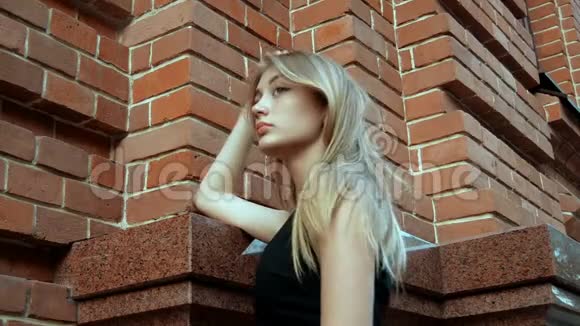 美丽的金发女郎站在砖房附近望着远处视频的预览图