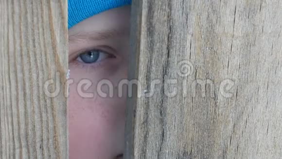 一个十几岁的男孩惊恐的蓝眼睛盯着门缝或栅栏的缝隙视频的预览图