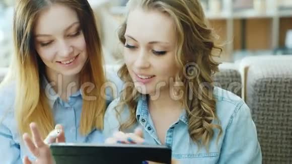 两个年轻迷人的女人在咖啡馆里使用平板电脑或笔记本电脑的肖像视频的预览图