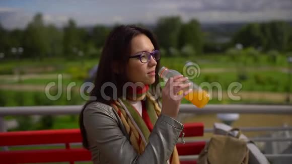 年轻漂亮的女人在户外夏天公园喝橙汁慢动作视频的预览图