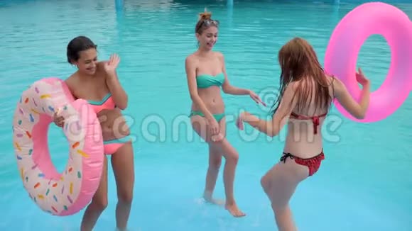 穿着泳装的年轻女子在泳池边翩翩起舞身穿粉色充气戒指的欢乐女孩视频的预览图