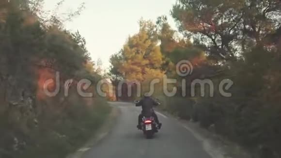 从后面的人骑摩托车在森林道路上库存黑色皮夹克摩托车手的美丽景色视频的预览图