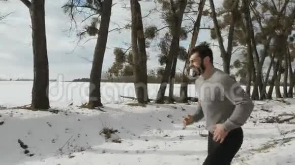 年轻的肌肉跑步者在路边的雪地上慢跑视频的预览图