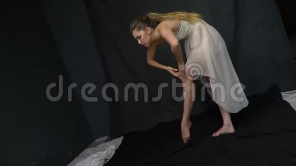 灵活的女孩修长的腿穿着白色连衣裙在演播室里摆姿势动作缓慢视频的预览图