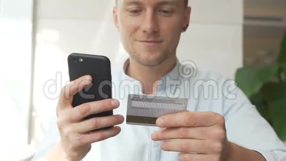 年轻人一手拿着信用卡另一手拿着智能手机购物视频的预览图