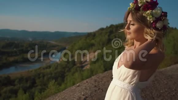 这位穿着白色波霍裙的美丽女子在壮丽的群山背景下触摸着花圈视频的预览图