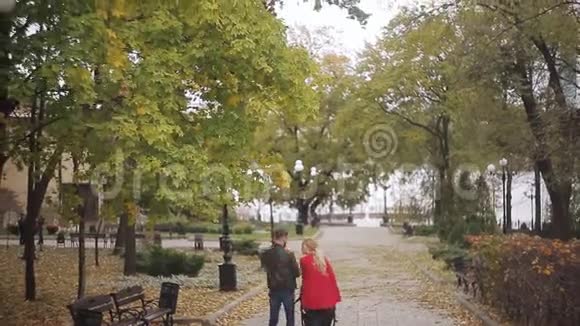 年轻的父母抱着一个孩子带着婴儿车漫步在秋天的公园里视频的预览图