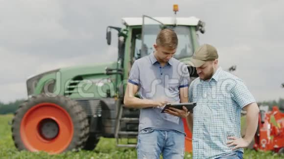 两个青年的农民沟通使用平板电脑站在拖拉机的背景下视频的预览图