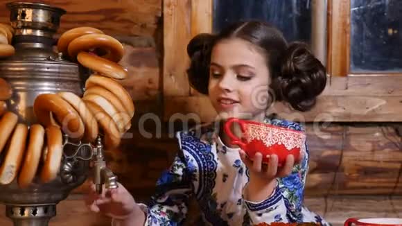 穿着传统服装的小漂亮女孩的肖像坐在古老的乡村木屋的桌子旁俄罗斯视频的预览图