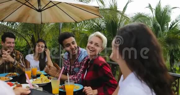 人们在餐桌上闲坐在户外吃饭年轻的朋友小组快乐的微笑近距离交流视频的预览图